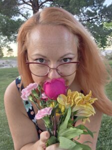 Nikki Ivana, Las Vegas escort, playfully looking over her sunglasses while holding flowers